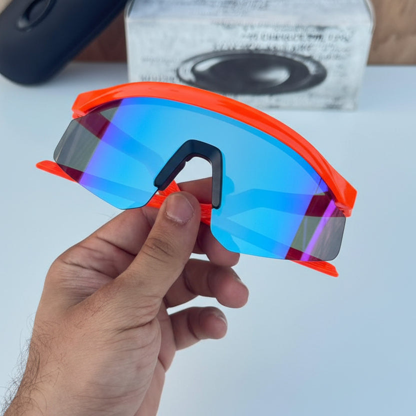 Hand holding a pair of sunglasses with reflective lenses on a white surface with Oakley branding.