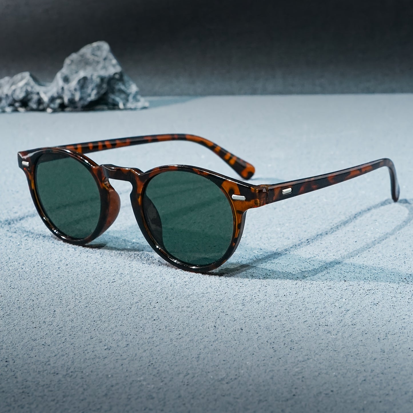 Sunglasses with tortoiseshell frame and dark lenses on a textured surface