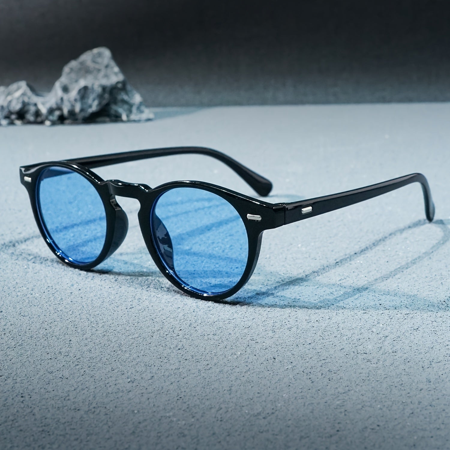 Black-framed sunglasses with blue lenses on a textured surface