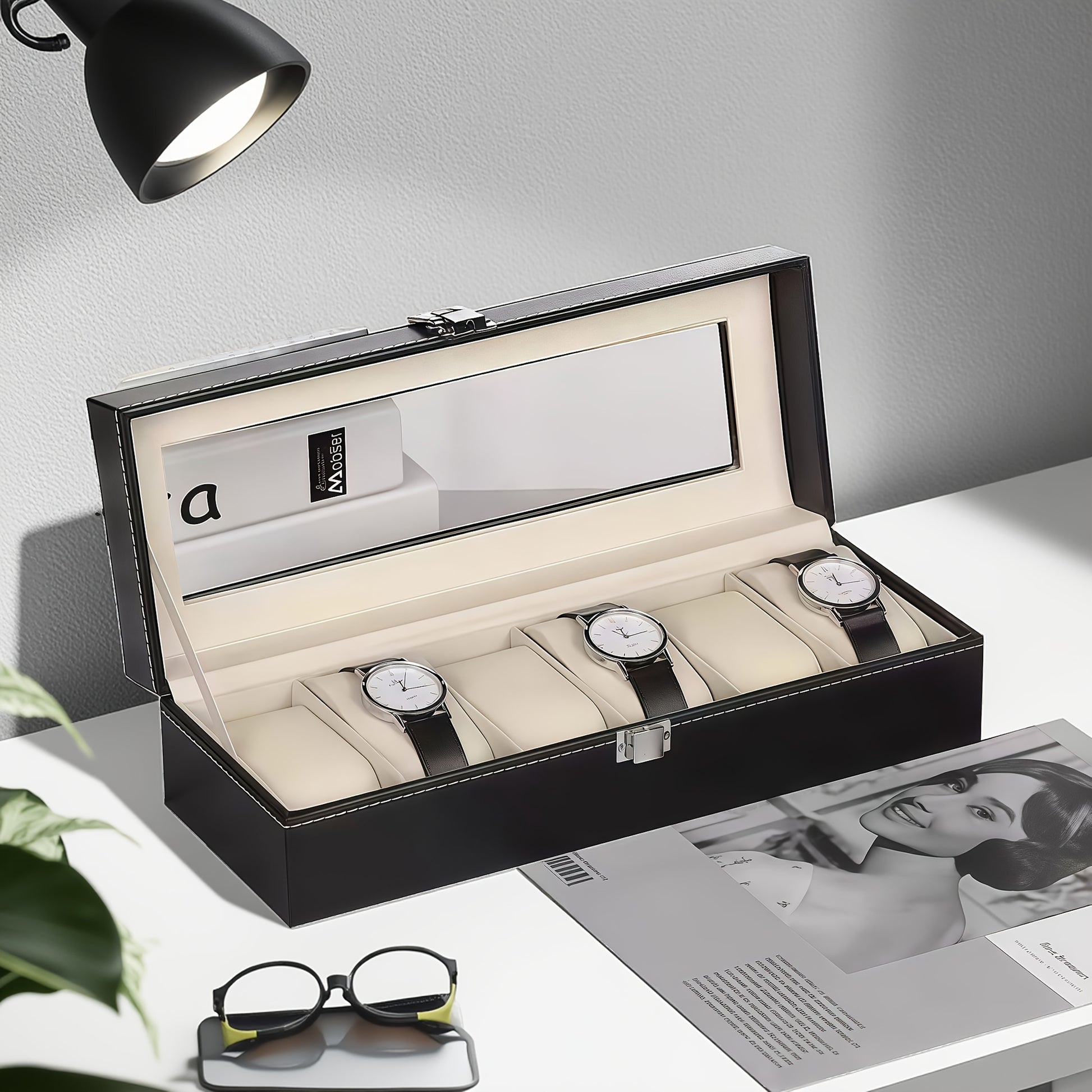 Black watch box with three watches on a table with a lamp and magazine in the background