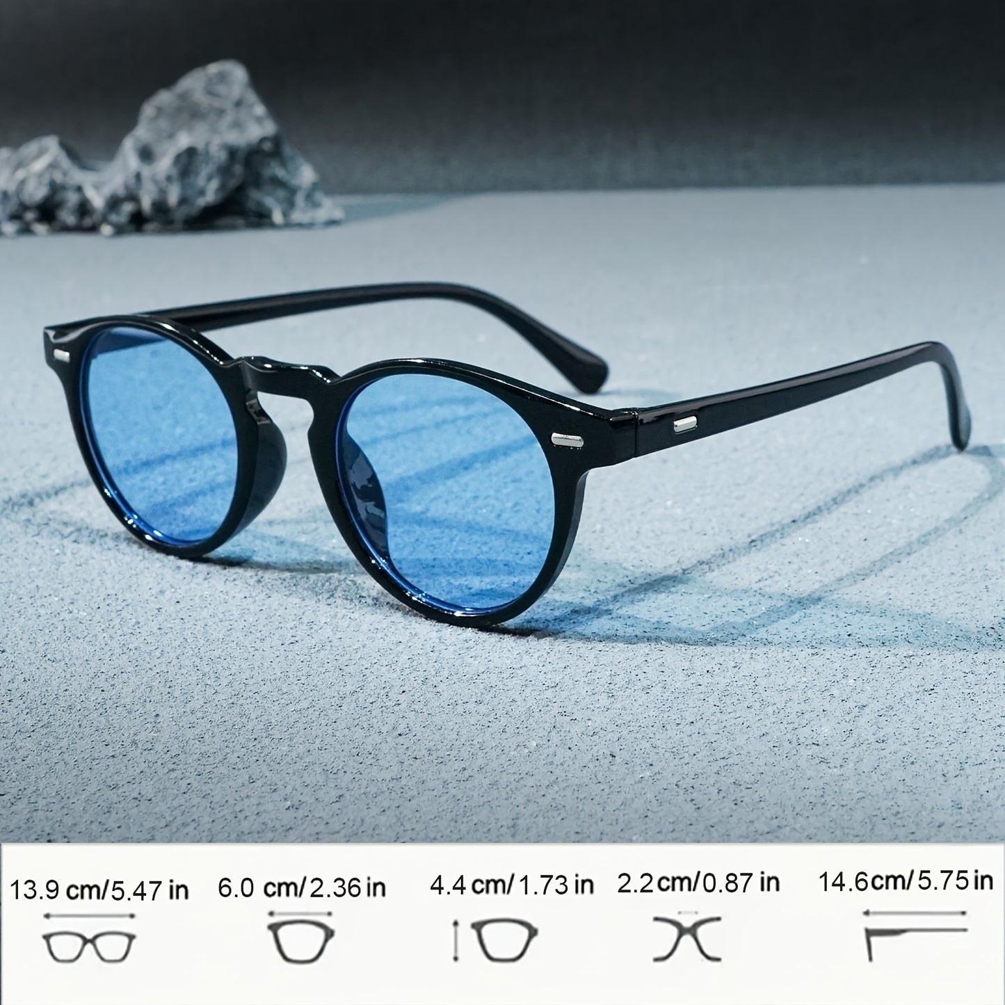 Black sunglasses with blue lenses on a sandy surface with rocks in the background