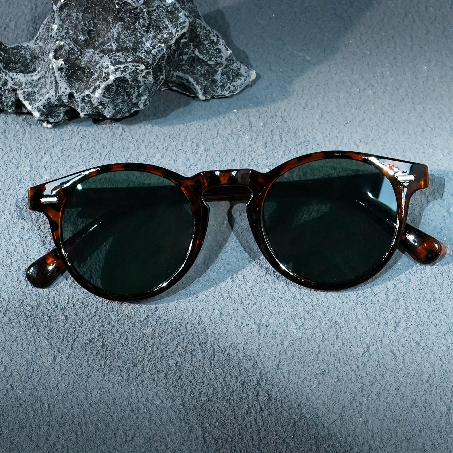 Round sunglasses with tortoiseshell frame and dark lenses on a textured gray surface.
