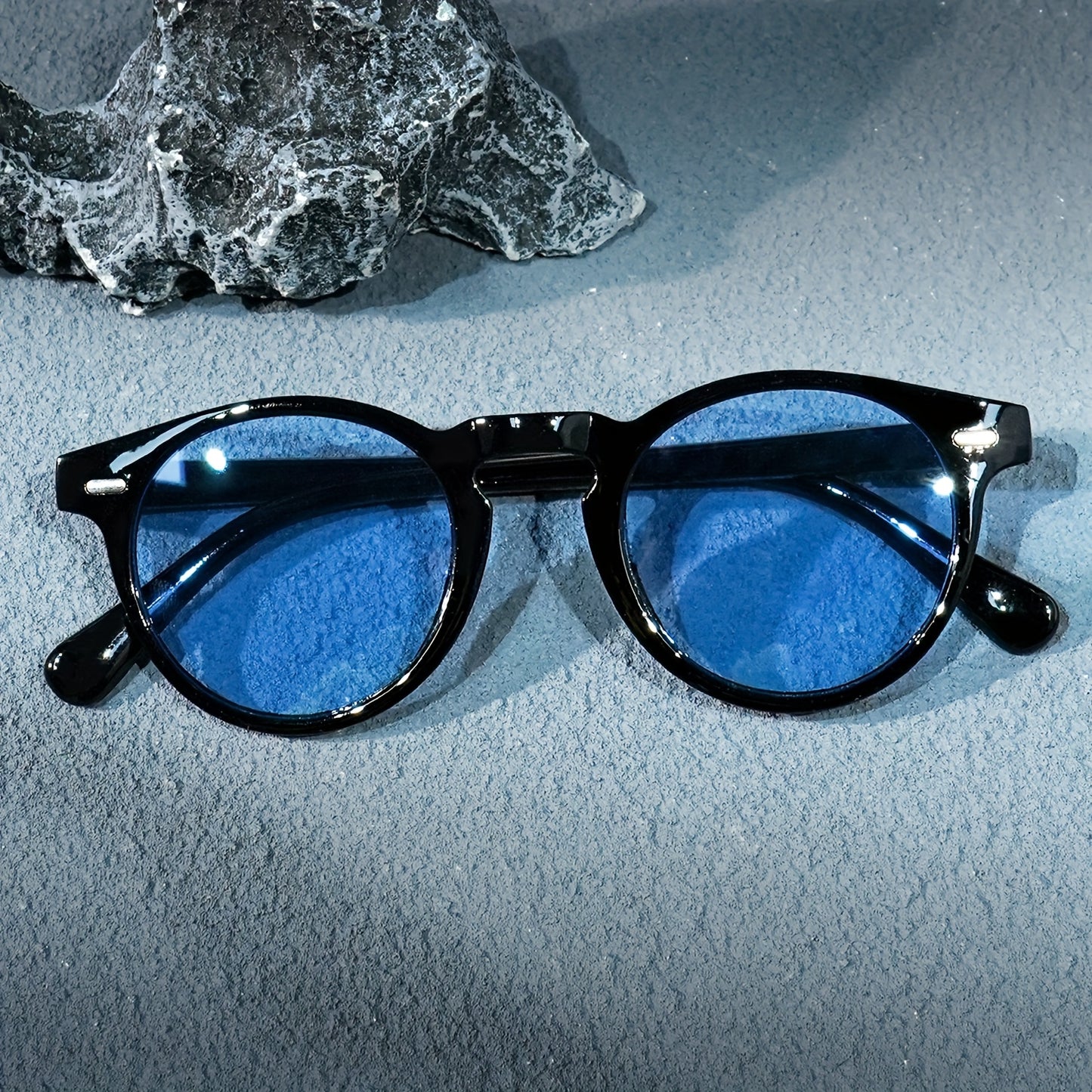 Black-framed sunglasses with blue lenses on a textured surface