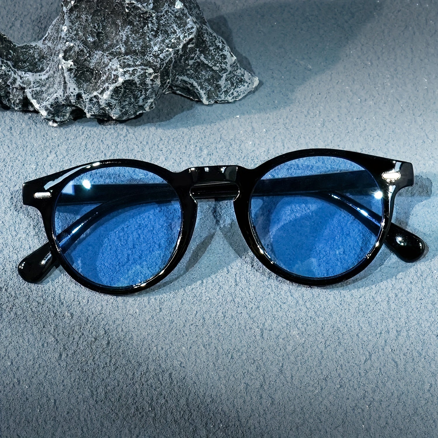Black-framed sunglasses with blue lenses on a textured surface