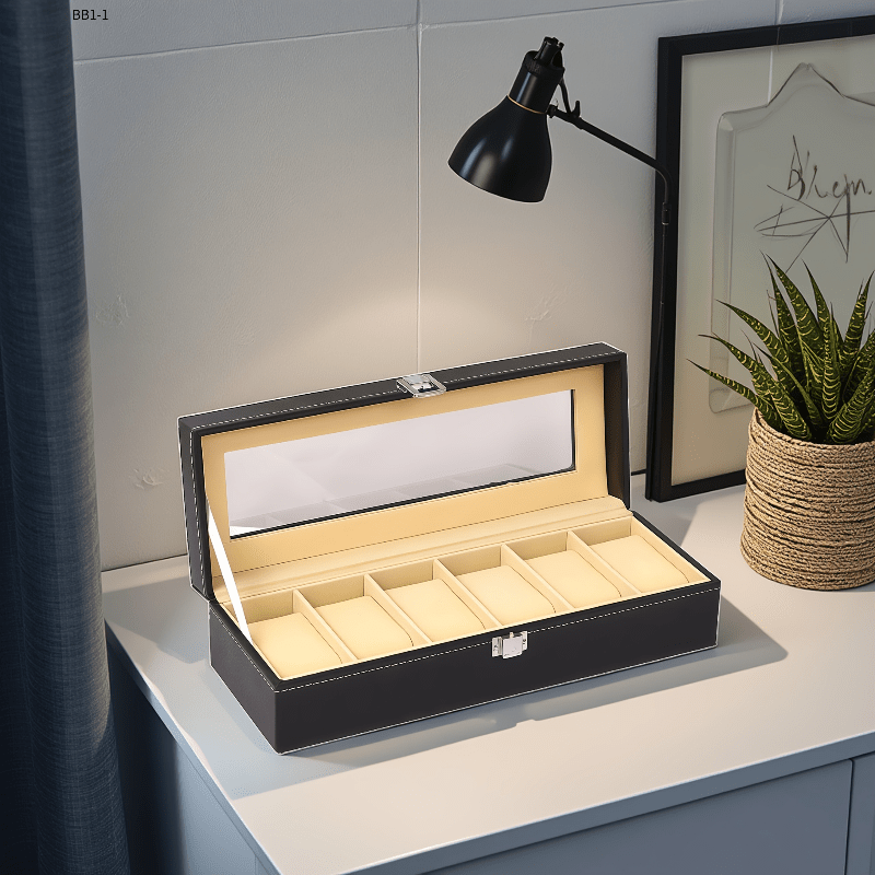Black jewelry box with beige interior on a white surface, lamp, and plant in the background.