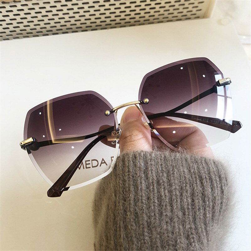 oversized rimless sunglasses for women with purple gradient lenses and gold bridge held by hand in gray sweater