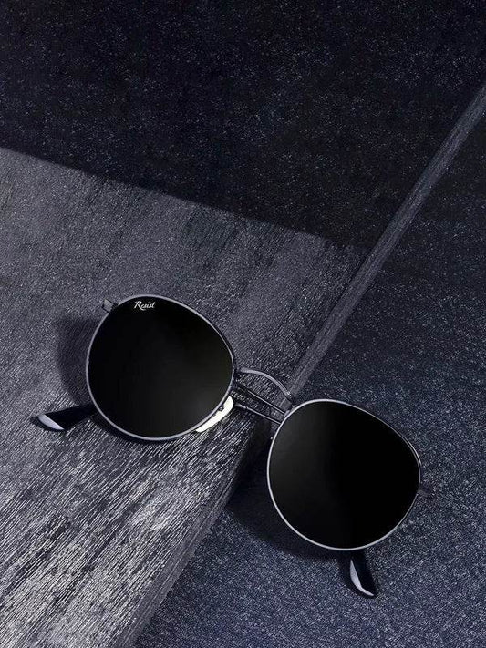 Sunglass Lover round black sunglasses with thin metal frame and dark lenses on textured surface