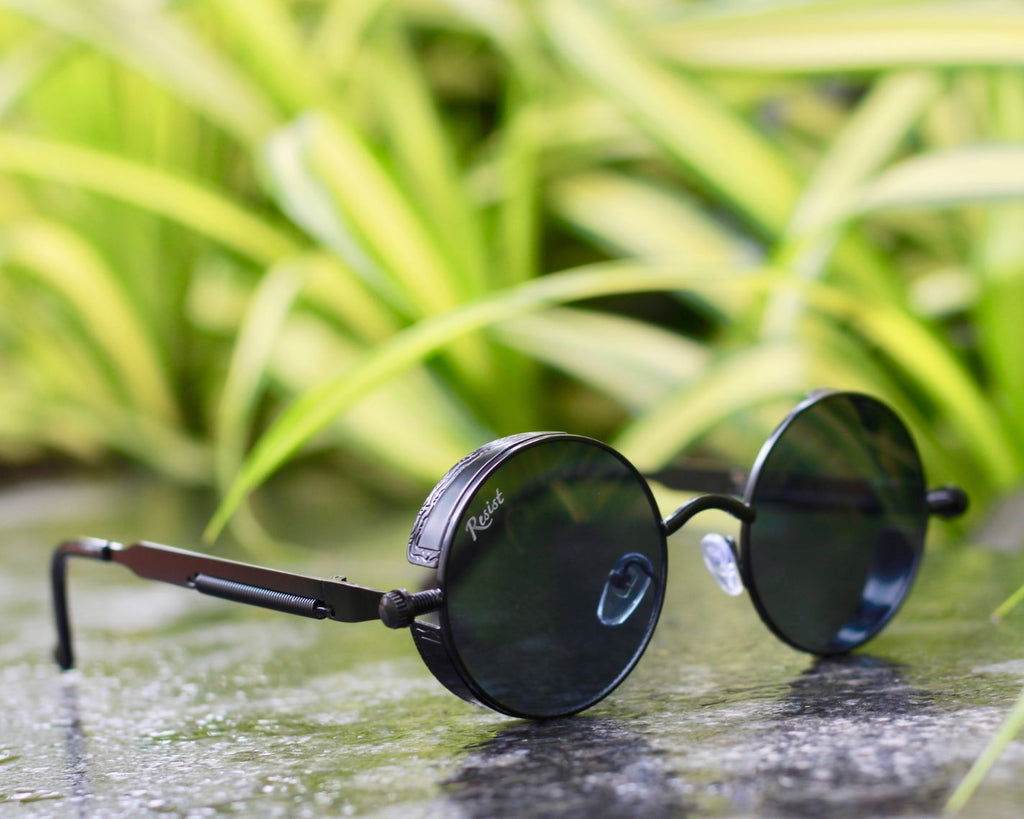Sunglass Lover black steampunk round sunglasses for men on wet stone with green foliage background