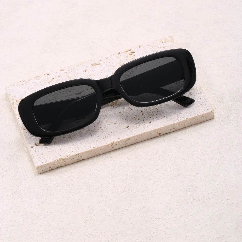 Black Jimmy Rectangle sunglasses by Sunglass Lover resting on textured stone slab with dark lenses
