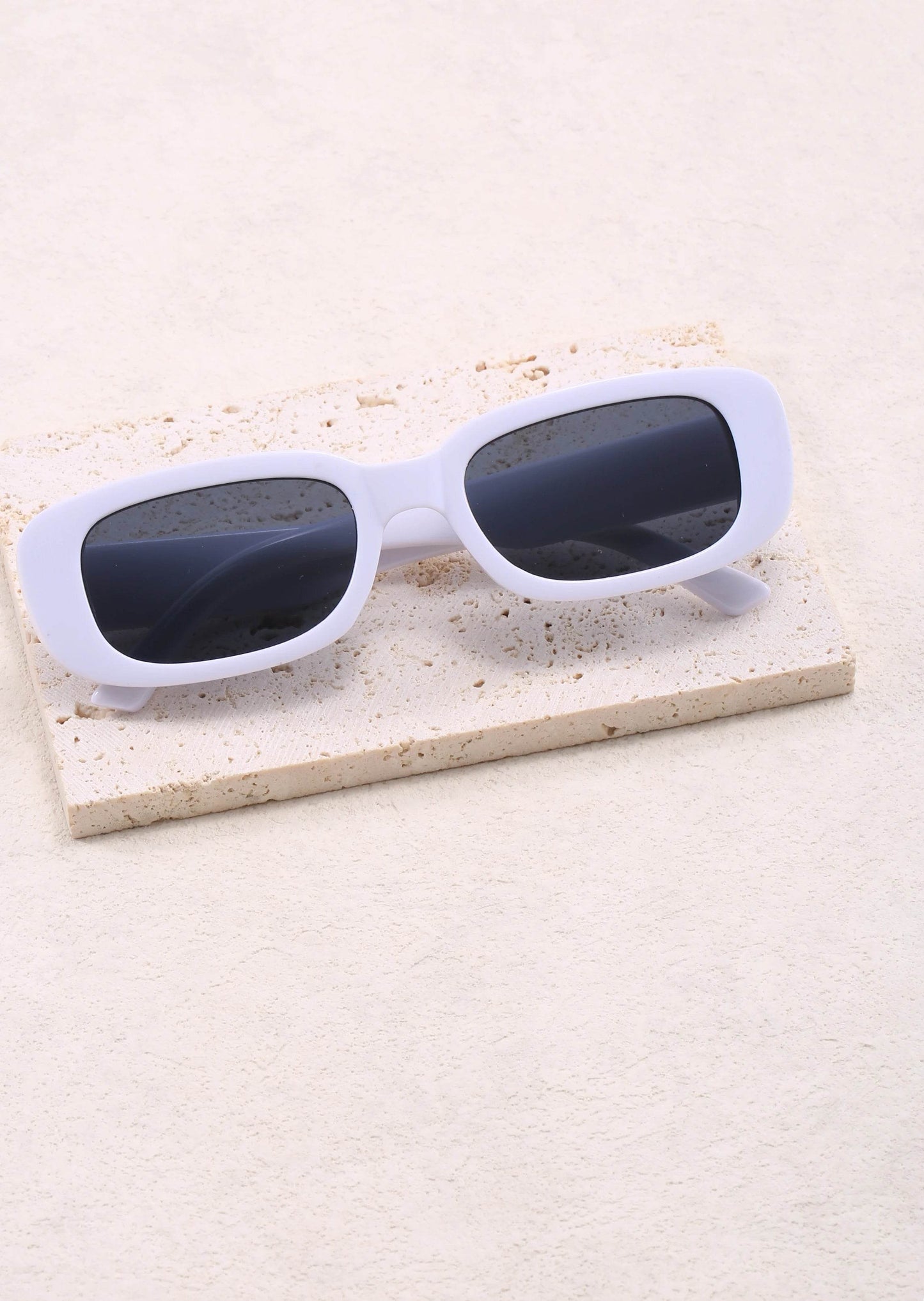 Sunglass Lover Jimmy Rectangle sunglasses white chunky frame with dark lenses on textured stone prop