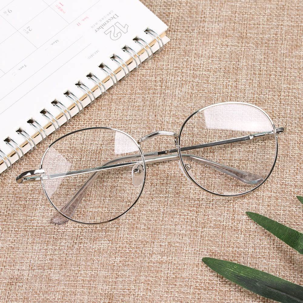 round metal frame reading glasses silver wire frames on beige woven surface beside spiral notebook and plant