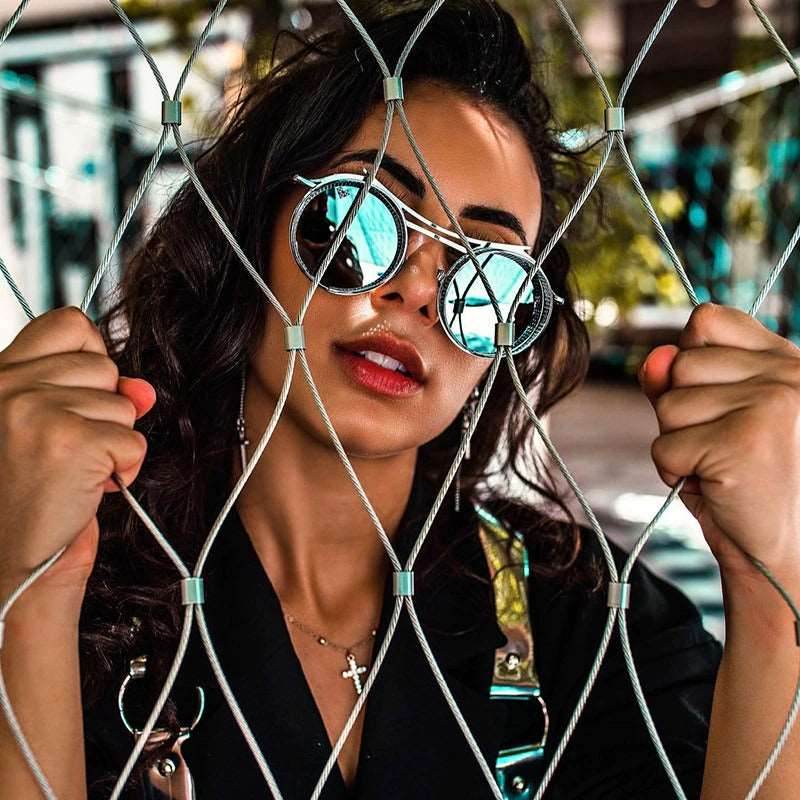 Sunglass Lover model wearing round steampunk sunglasses with blue mirrored lenses behind fence