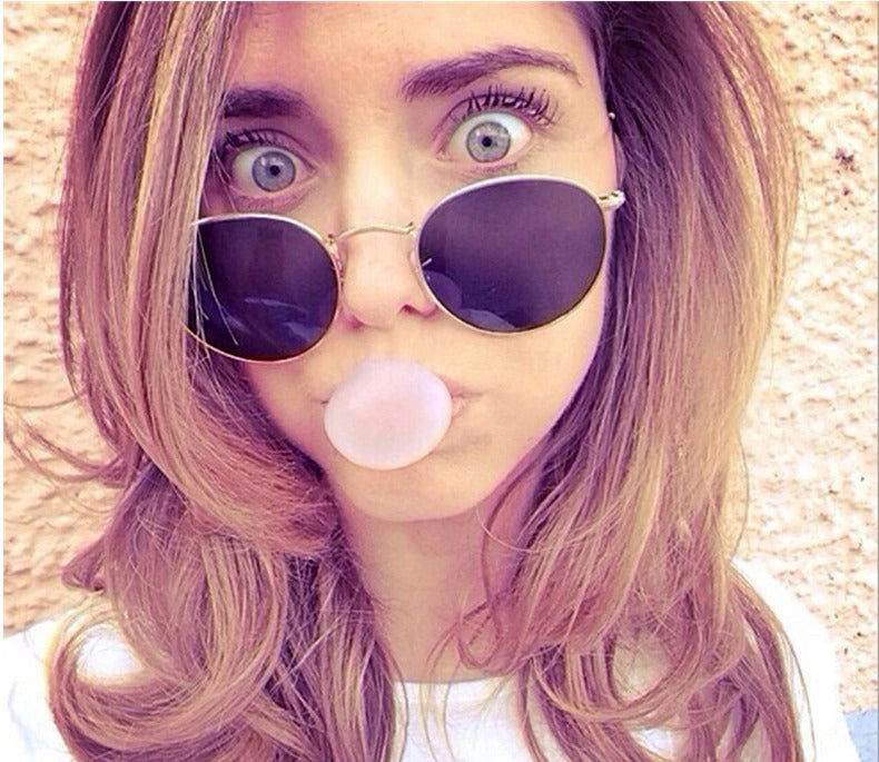 Round gold frame sunglasses with dark lenses on woman blowing gum casual style round sunglasses for men and women