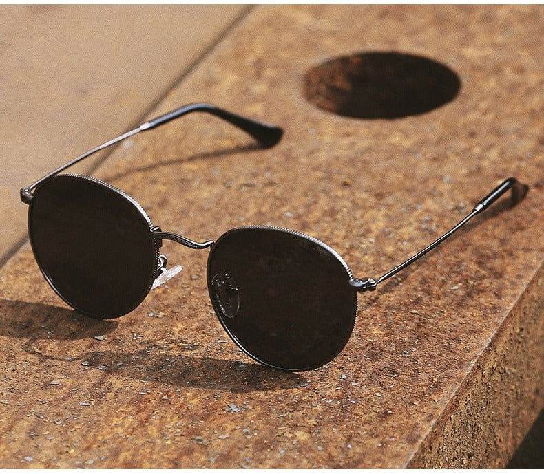 Sunglass Lover silver metal frame with black round lenses round sunglasses for men and women resting on textured stone surface