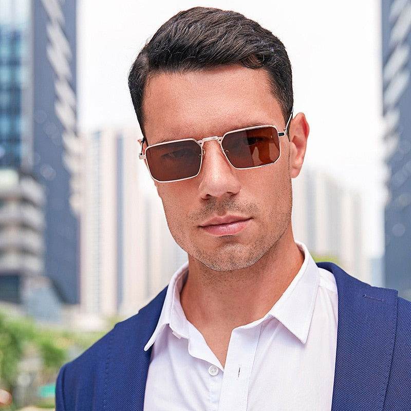 Man wearing square retro sunglasses with gold metal frame and brown lenses in urban business outfit