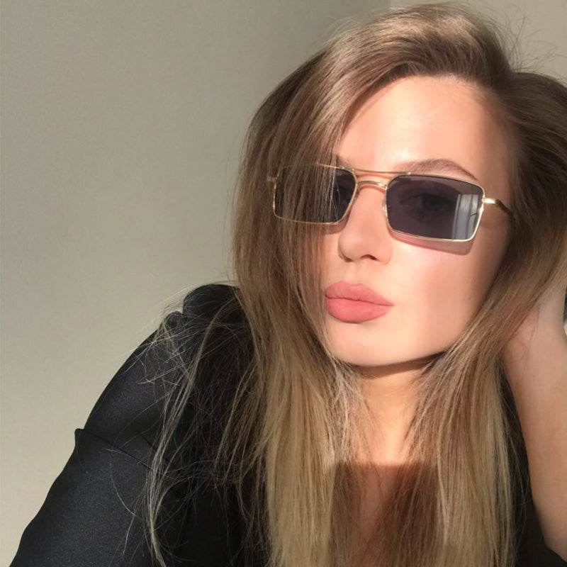 Sunglass Lover woman wearing gold frame double bridge rectangle sunglasses with dark lenses and sleek design