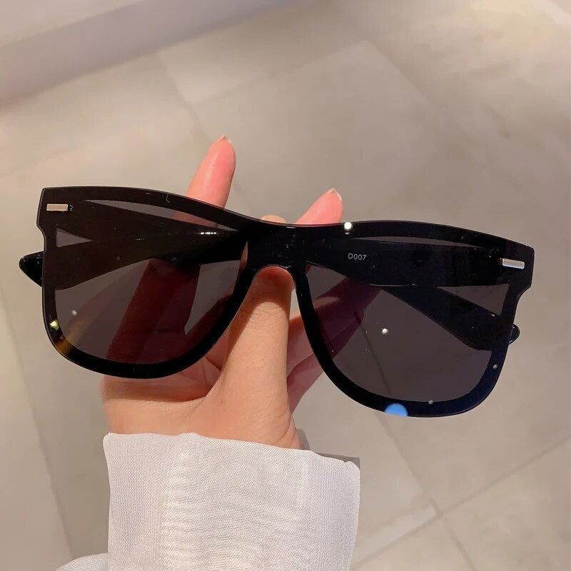 Sunglass Lover rimless oversized square sunglasses in black held by hand showing large dark lenses