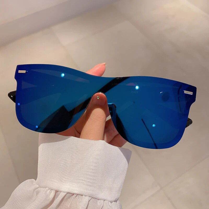 Sunglass Lover rimless oversized square sunglasses with blue mirrored lenses held by hand in white sleeve