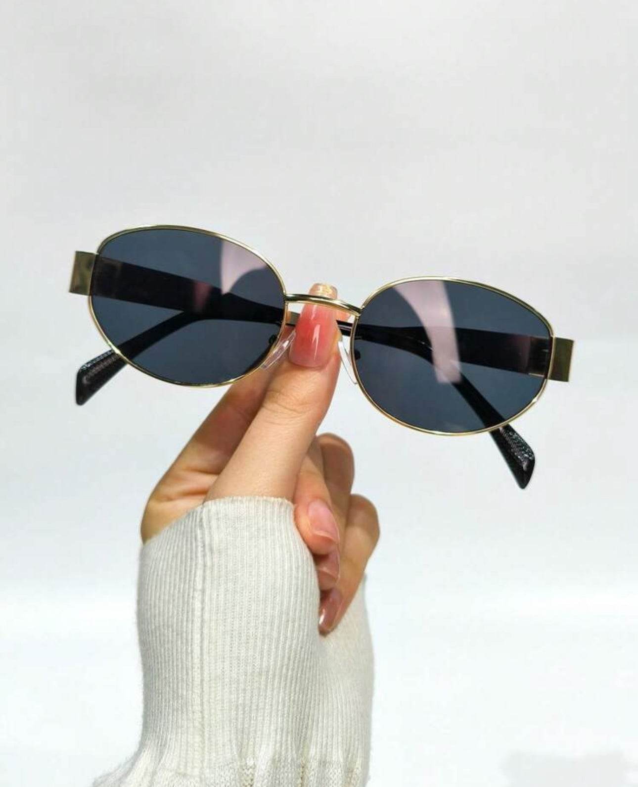 Sunglass Lover gold frame oval sunglasses with black lenses held by hand in white sweater fashion oval sunglasses online India