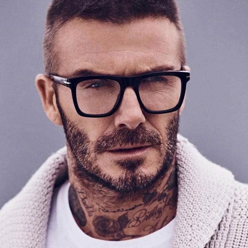Man wearing black frame blue light blocking square glasses with knitted sweater and neck tattoos