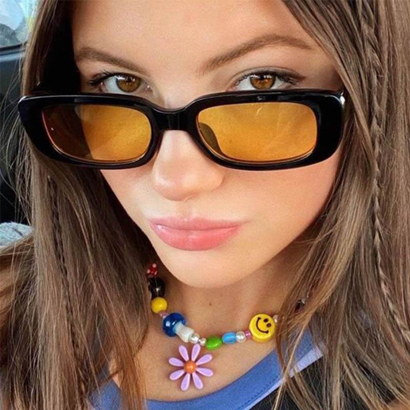 Young woman wearing retro rectangle sunglasses for women with black frames amber lenses and colorful beaded necklace