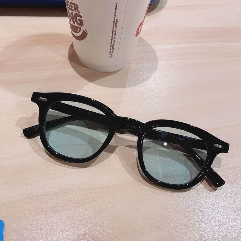 Sunglass Lover black acetate vintage round sunglasses for men and women with green tinted lenses on table